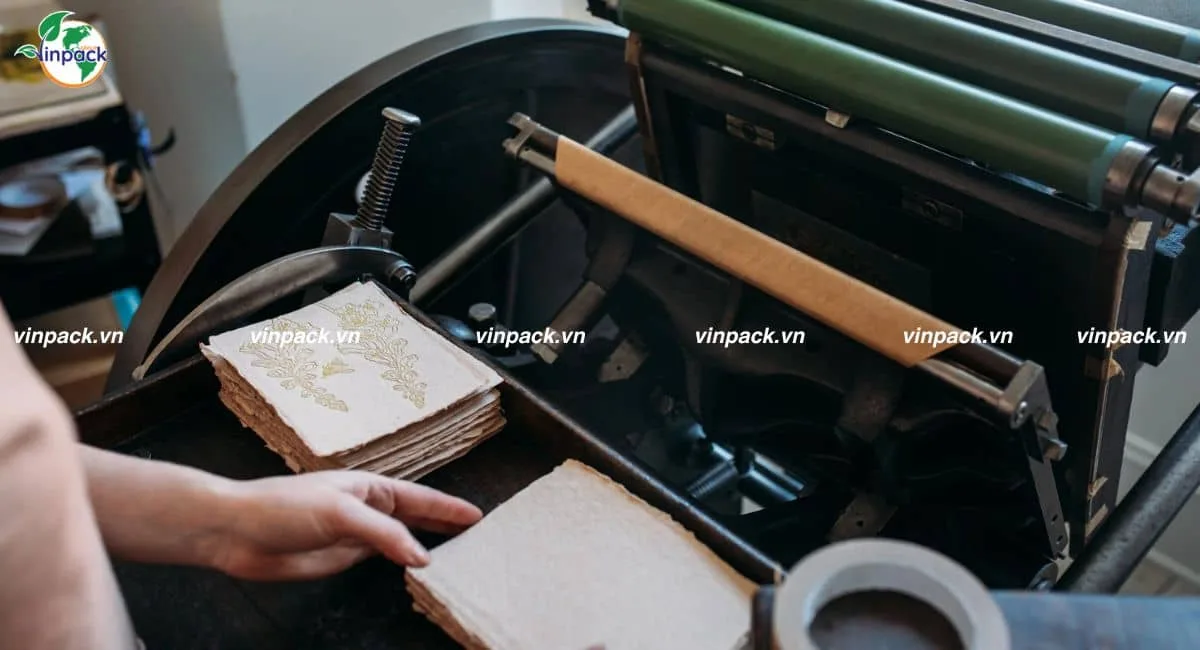 Xấp giấy mỹ thuật in họa tiết vàng bên cạnh máy in letterpress